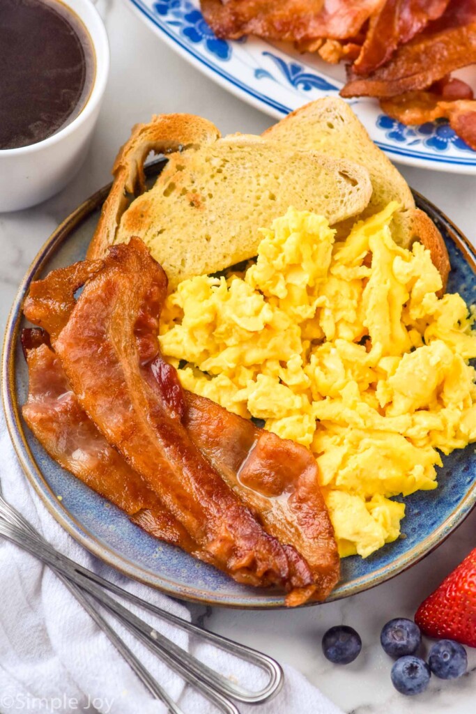 plate of Bacon in The Oven, scrambled eggs, and toast. Plate of bacon, fresh berries, and a mug of coffee sitting beside