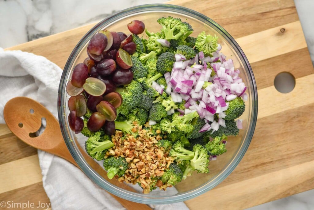Overhead view of mixing bowl of ingredients for Broccoli Salad recipe. Wooden spoon beside.