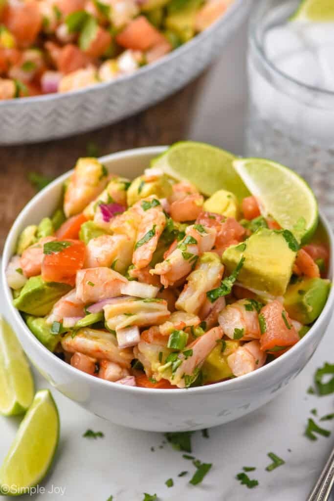 a small bowl full of shrimp avocado salad and garnished with two lime wedges