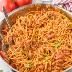 skillet of Taco Spaghetti with two forks for serving. Tomatoes and drinking glass sitting in background - 10