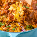 Pinterest graphic for Chili Mac. Image shows wooden spoon in pot of Chili Mac topped with melted cheese, fresh cilantro, and diced red onion. Text says "super easy Chili Mac recipe simplejoy.com"