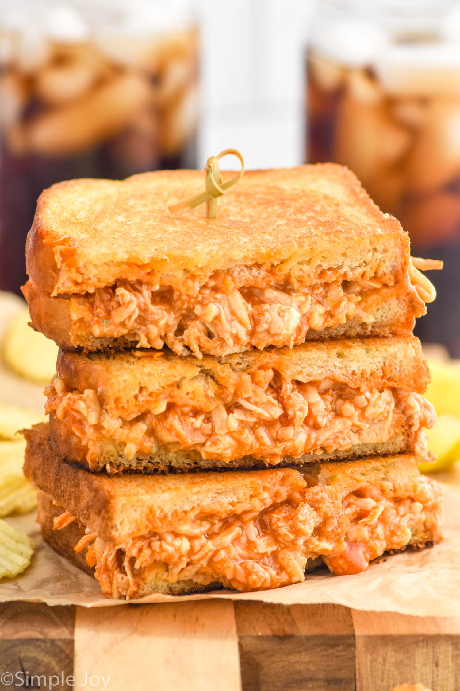 Stack of Buffalo Chicken Sandwich halves with potato chips sitting in background