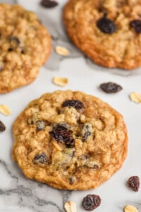 an oatmeal raisin cookie on a counter top with two cookies near it