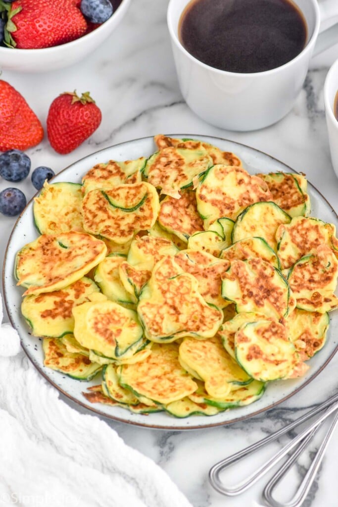 Plate of Italian Zucchini Fritters with fresh strawberries and blueberries and mug of coffee sitting beside