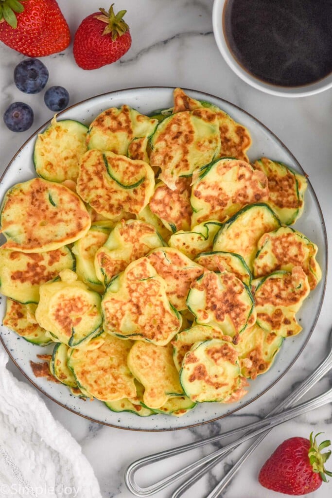 overhead of Italian Zucchini Fritters on a plate with fresh blueberries, strawberries, and mug of coffee surrounding