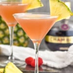 two glasses of French Martini garnished with a pineapple wedge. Fresh pineapple, raspberries, and bottle of Chambord liqueur sitting in background - 6