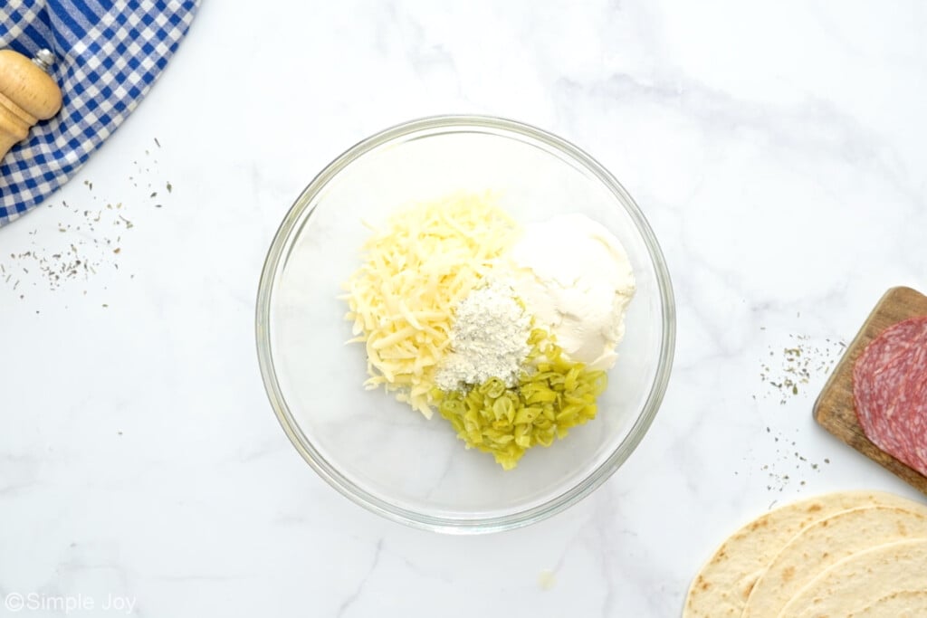 overhead of a bowl of cream cheese, cheese, pepperonchinis, and italian seasoning to make italian pinwheels - 5