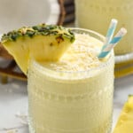 Glass of Pina Colada Smoothie topped with shredded coconut, garnished with a pineapple wedge and two straws. - 9
