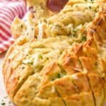 Man's hand pulling piece of Pull Apart Bread from loaf that is topped with melted cheese and fresh parsley - 9