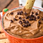 Person's hand dipping cracker into bowl of Pumpkin Nutella Dip garnished with mini chocolate chips. More dipping crackers beside bowl. - 15