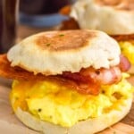 Breakfast Sandwich with slices of bacon, eggs, and cheese on an english muffin. Breakfast Sandwich and mugs of coffee sitting in background - 6