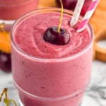 angled view of a cherry smoothie in a glass with a cherry on top and two paper straws - 8