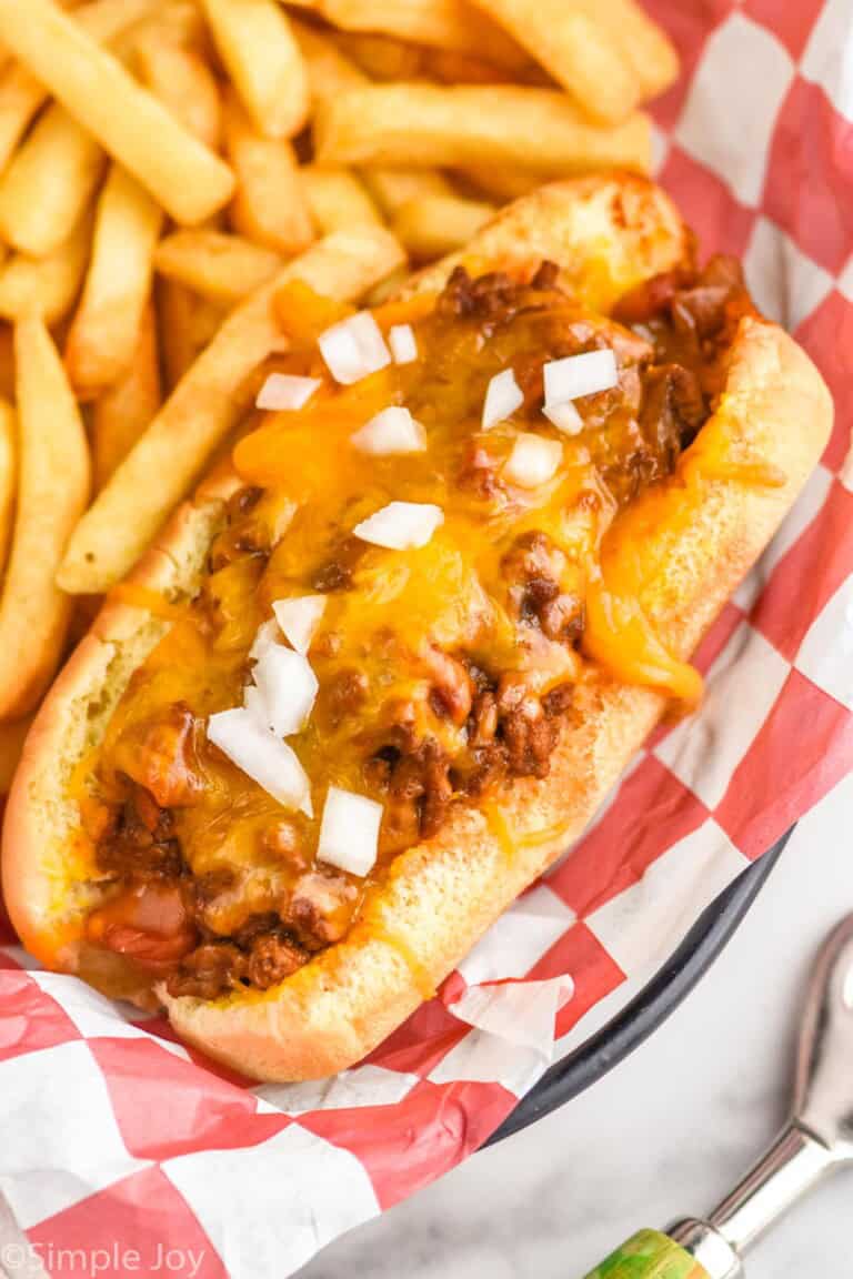 Chili Dogs topped with diced onion with french fries sitting beside
