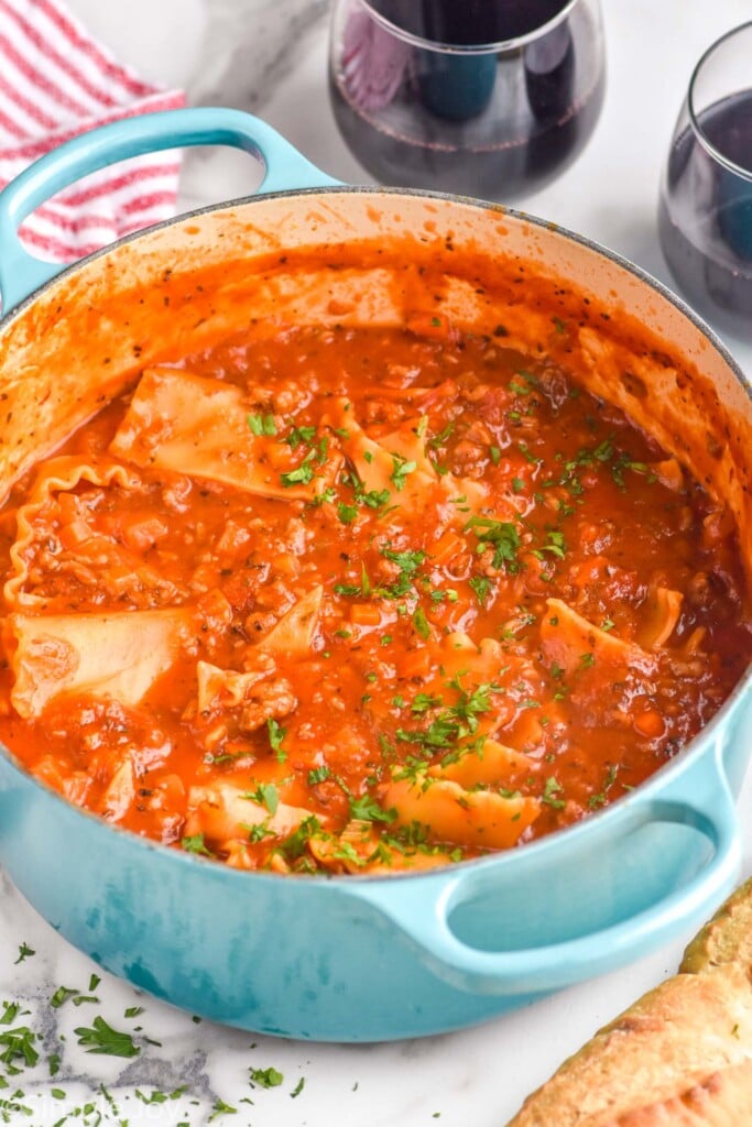 large pot of Lasagna Soup topped with fresh parsley. Two glasses of red wine sitting in background