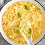 hand holding spoon of Egg Drop Soup over a bowl of Egg Drop Soup topped with diced green onions - 8