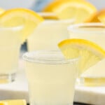 Shot glass of Lemon Drop Shot with sugared rim and slice of lemon for garnish. Lemon Drop Shots sitting in background, slices of lemon sitting beside - 8