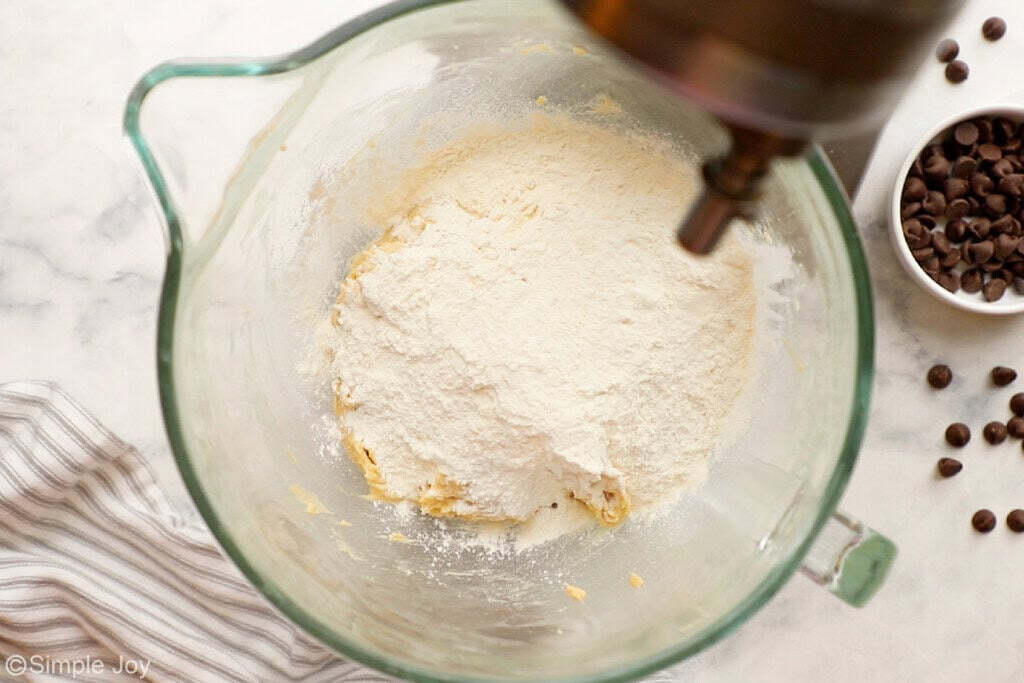 flour being added to creamed butter and sugar to make cookie batter