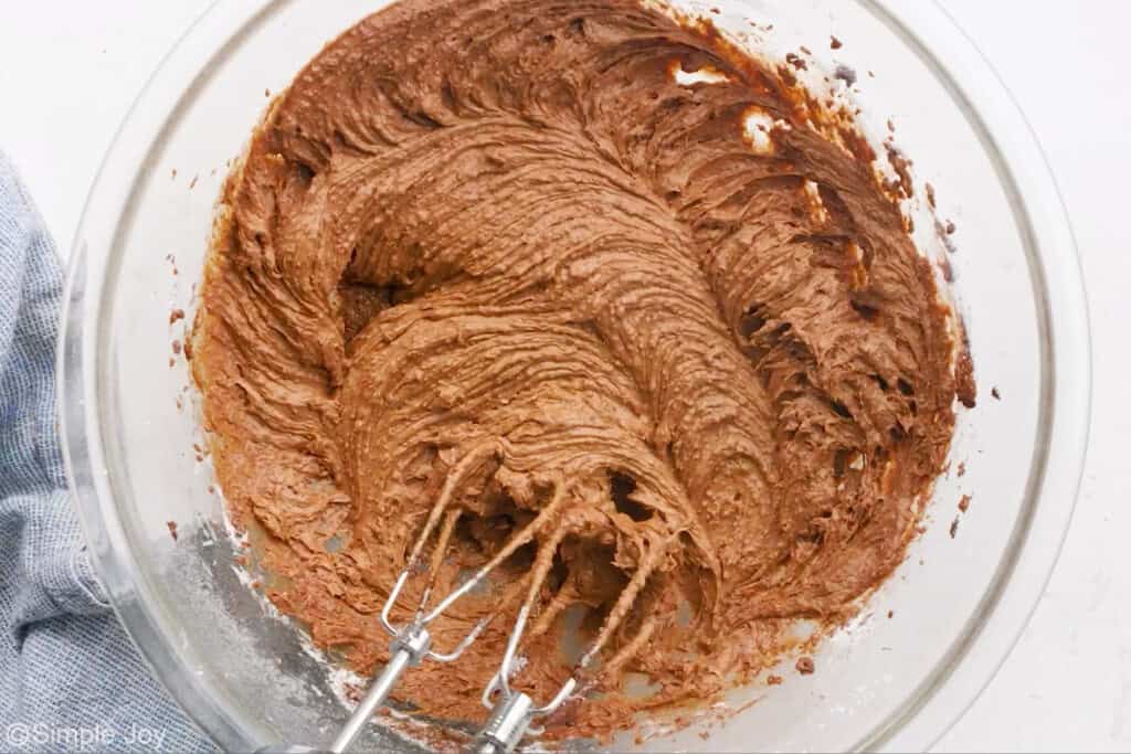 overhead of a bowl of chocolate frosting with beaters from a mixer in it