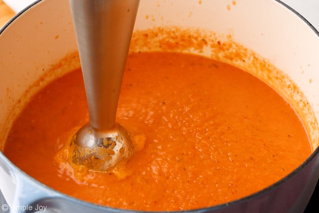an immersion blender blending tomato soup in a soup pot