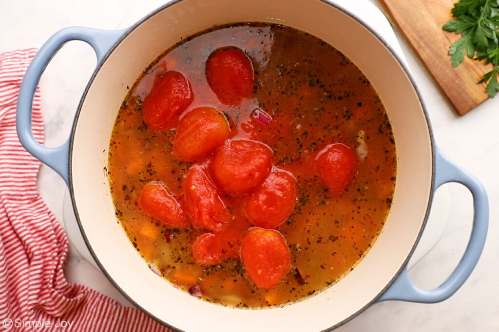 overhead of whole tomatoes and chicken broth in a soup pot