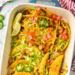 Pinterest graphic for baked tacos. Text says "the best baked tacos simplejoy.com" image shows overhead of casserole dish of baked tacos topped with melted cheese, shredded lettuce, diced tomatoes, and diced Jalapeños.