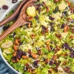 bowl of Shaved Brussels Sprout Salad topped with shredded parmesan cheese, walnuts, and dried cranberries with two wooden spoons for serving. - 7