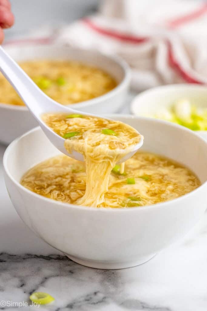 side view of a bowl of egg drop soup with a spoon dishing some up