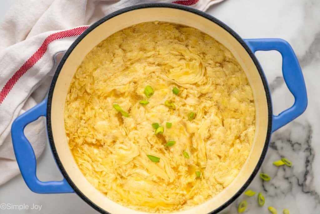 overhead of a stockpot with egg drop soup, garnished with green onions