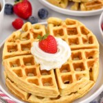 plate of homemade waffles topped with whipped cream and a strawberry. Fresh berries and plate of waffles sitting in background - 9