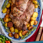 Pinterest graphic for Boneless Leg of Lamb Recipe. Image shows overhead of Boneless Leg of Lamb on a platter surrounded by potatoes and rosemary sprigs. Text says "tried and tested roasted Leg of Lamb simplejoy.com"