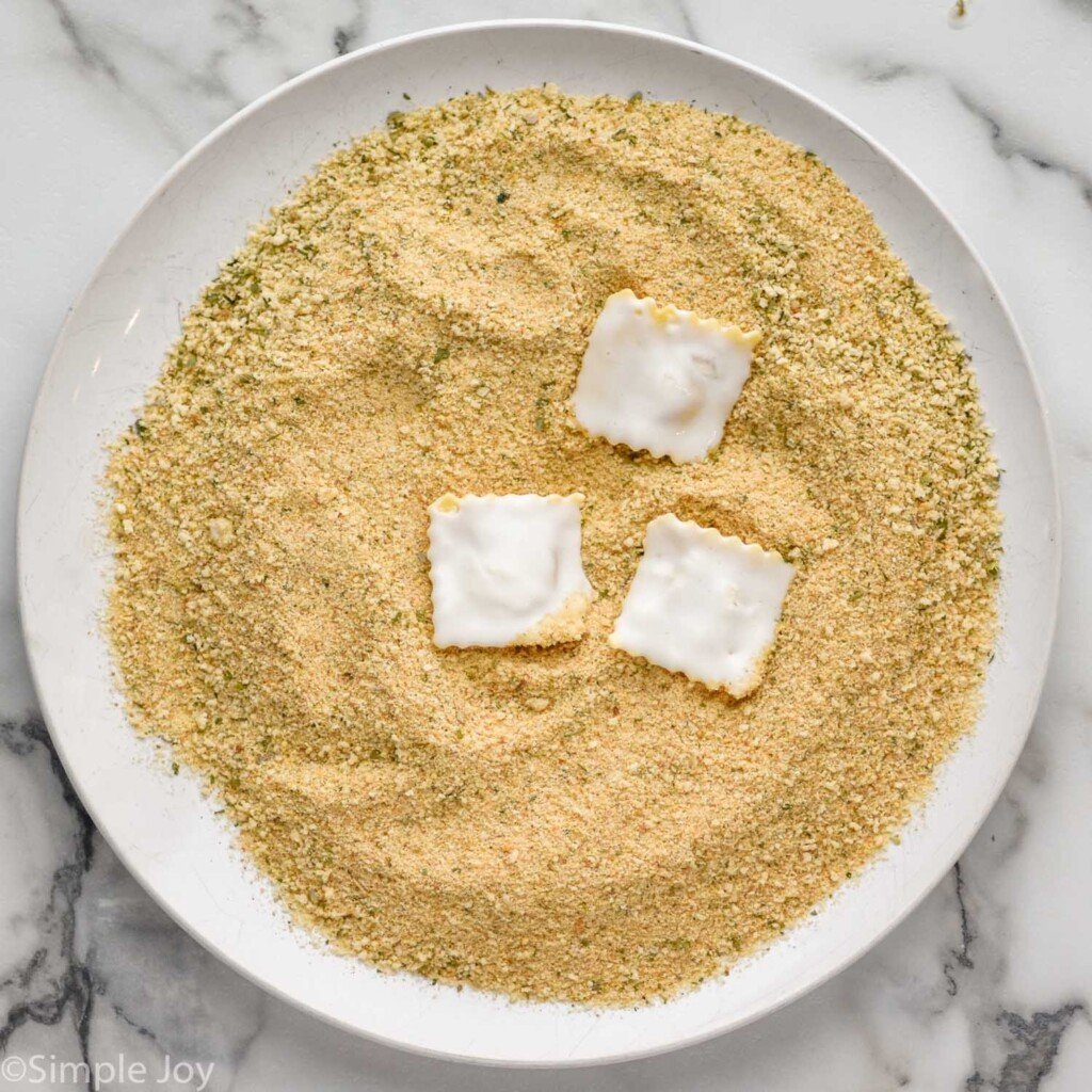 plate of Italian seasoning breadcrumbs with three ravioli on top to make Fried Ravioli