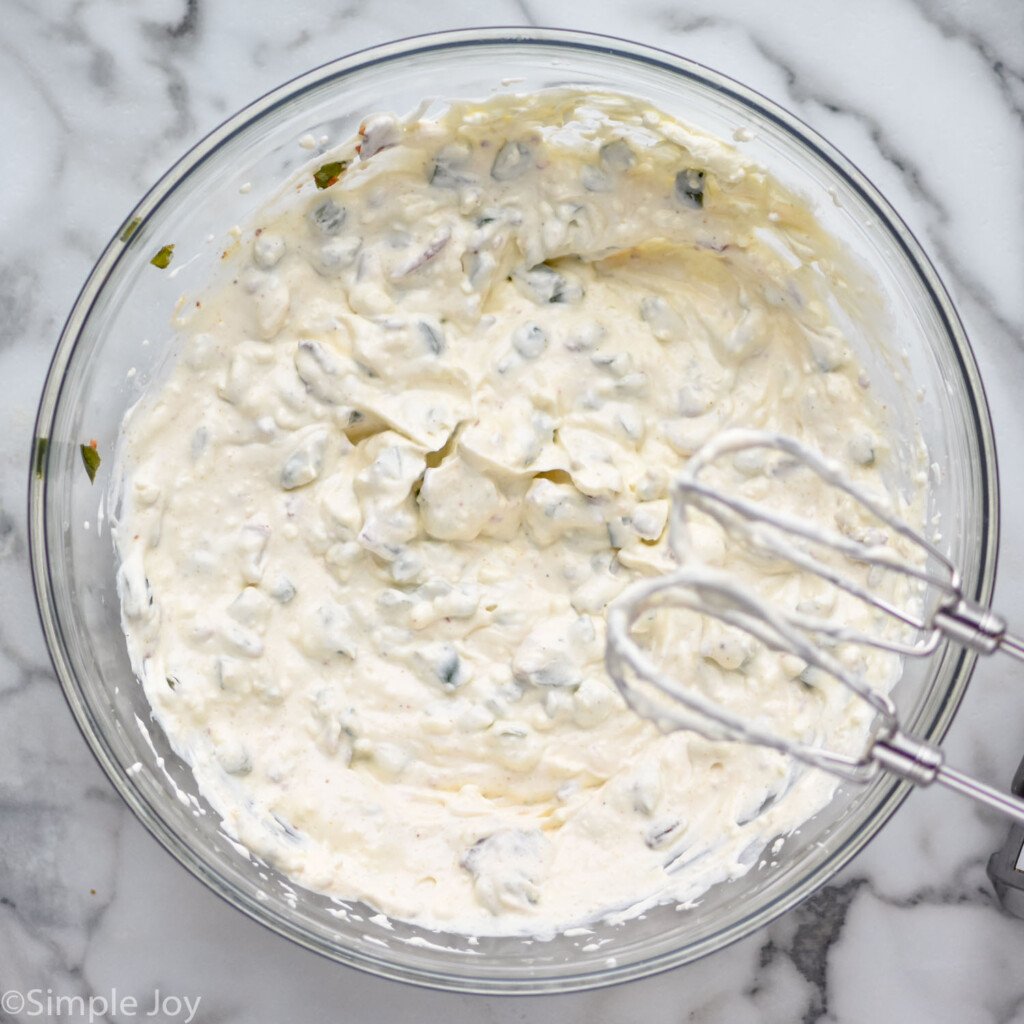 overhead of glass bowl of Jalapeño Popper Dip ingredients with beaters overhead