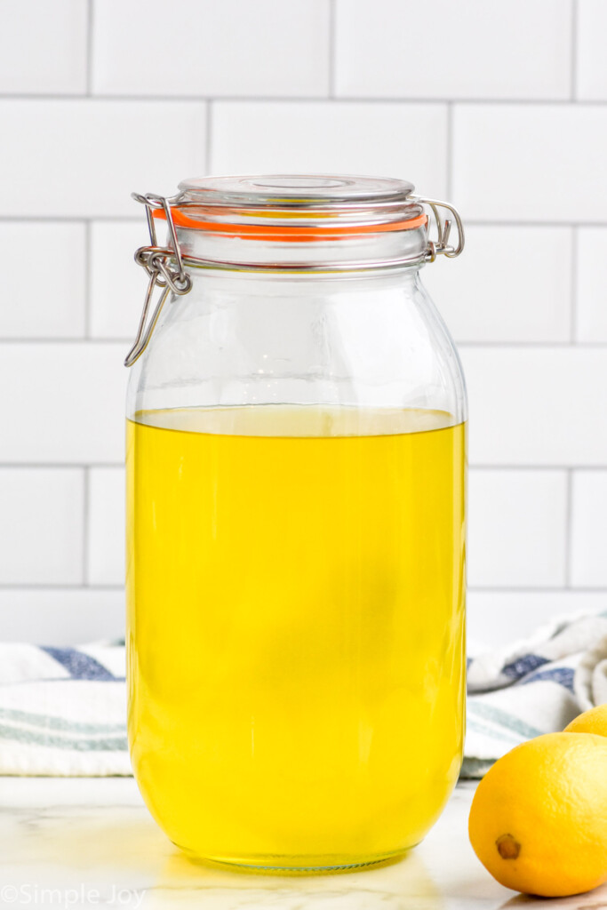 Side view of a jar of Limoncello recipe. Lemons on counter beside.
