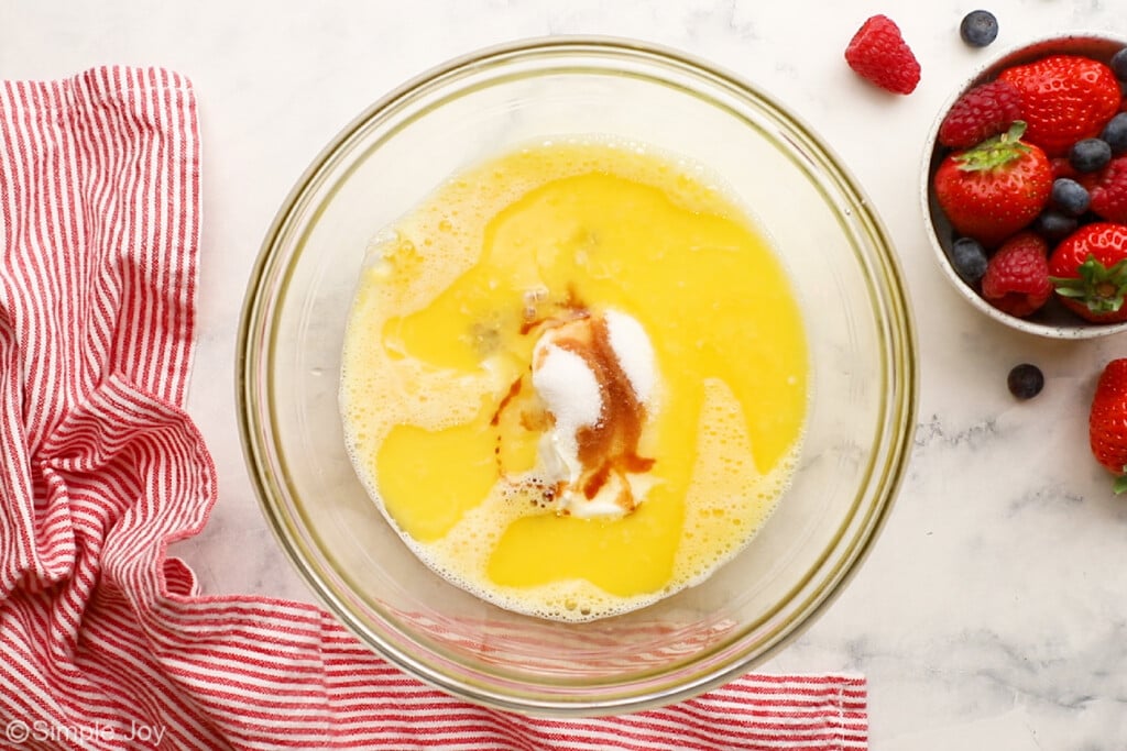 overhead of a bowl combining eggs, milk, sour cream, melted butter, sugar, and vanilla to make waffles