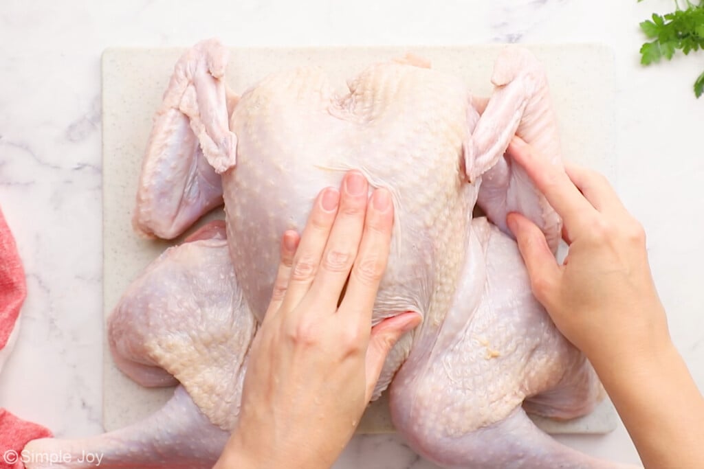 a hand pushing down on the breast bone of a turkey to break it and make it lay flat for spatchcock turkey - 7