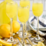 Side view of wine glasses with Limoncello. Jug of Limoncello behind with lemons and lemon slices beside on platter. - 12
