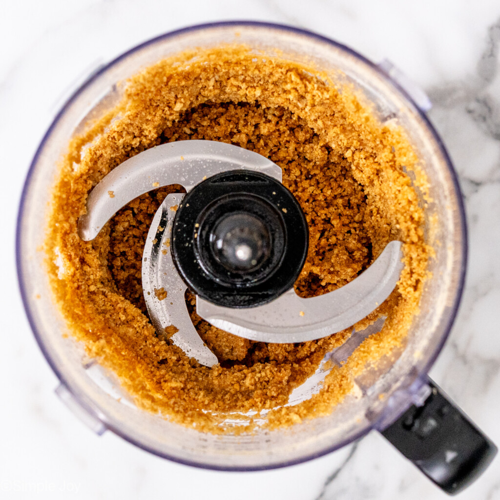 overhead of graham cracker crumbs mixed with butter in a food processor