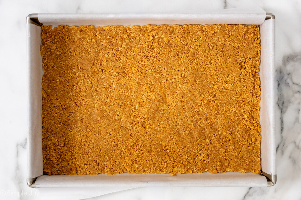 overhead of a 9 by 13 inch baking dish lined with parchment paper with a graham cracker crumb butter mixture pressed in