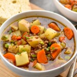 Bowl of Vegetable Beef Soup with spoons and piece of bread sitting beside - 9