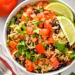 Overhead view of a bowl of Black Beans and Rice with diced tomatoes, cilantro, and lime wedges. Fork and tomatoes beside. - 8