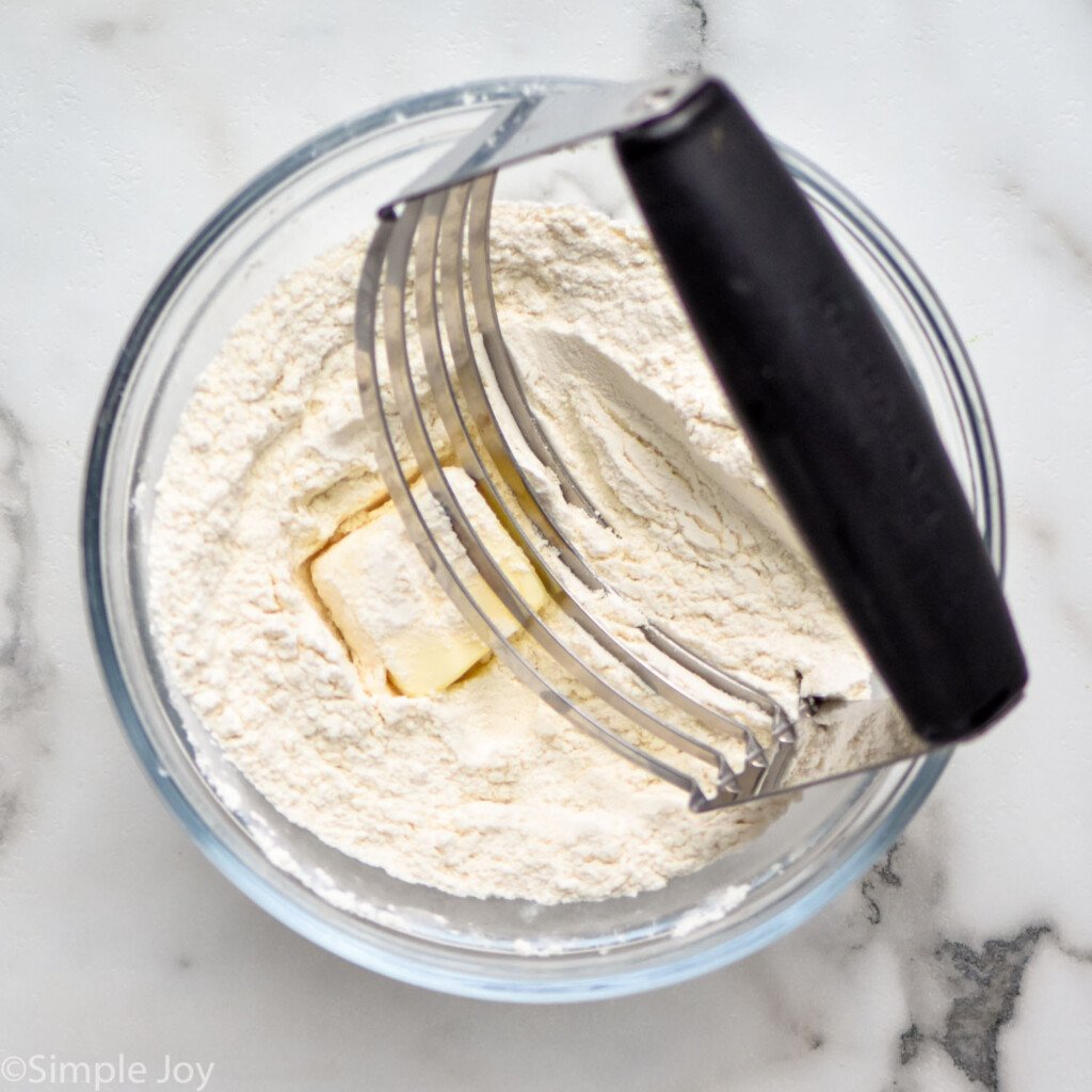 Overhead view of glass mixing bowl with flour, butter, and a pastry cutter for Crockpot Chicken and Dumplings recipe