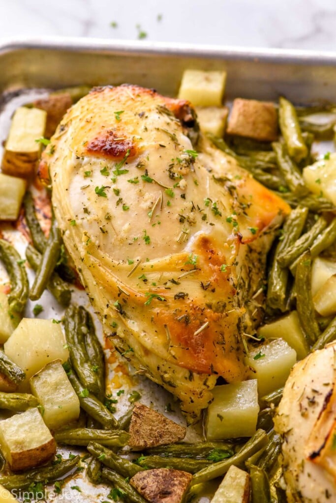 close up of a cooked cooked sheet pan chicken and veggies with potatoes and green beans around it