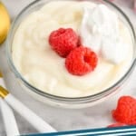 Pinterest graphic for Pudding recipe. Image shows a bowl of Pudding garnished with raspberries and whipped cream, raspberries and spoons beside. Text says, "the best Pudding simplejoy.com."