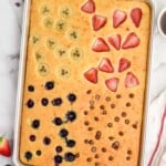 Overhead view of Sheet Pan Pancakes garnished with bananas, strawberries, blueberries, and chocolate chips in quadrants. Cup of coffee and berries beside. - 10