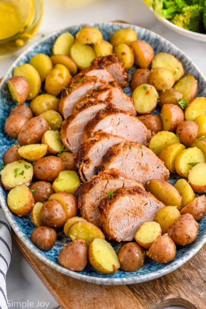 Platter of sliced Air Fryer Pork Tenderloin surrounded by cooked potatoes.