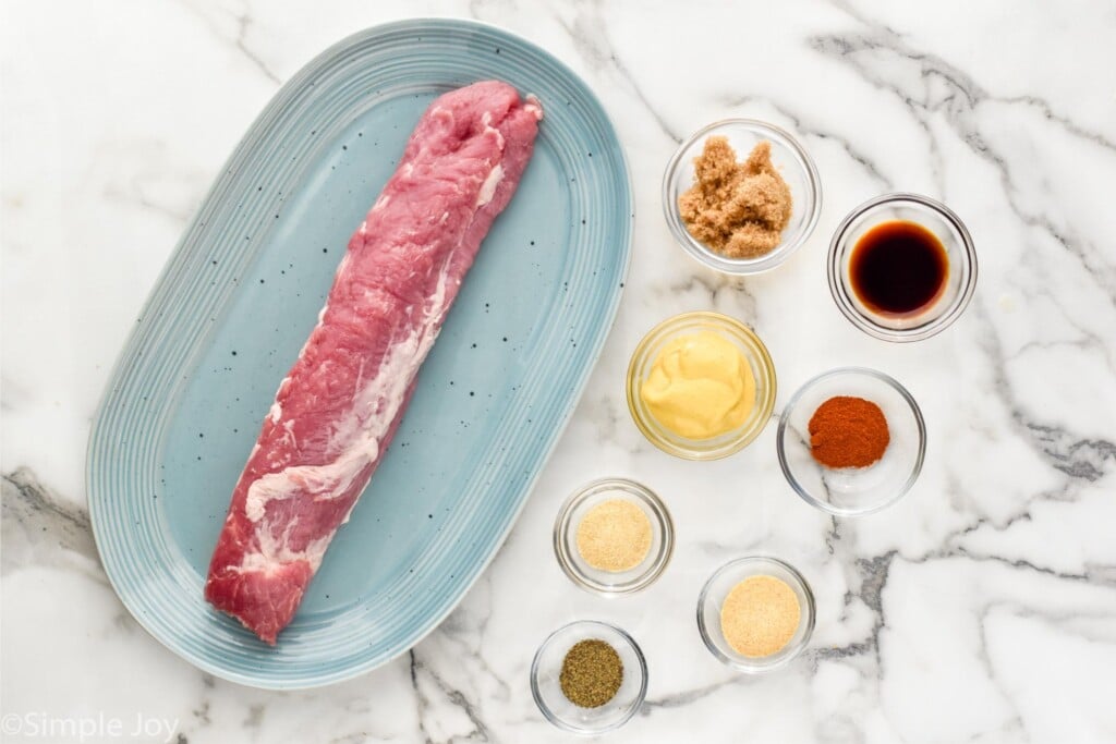 Overhead view of a platter with a raw pork tenderloin and small dishes of seasonings beside for sauce for Air Fryer Pork Tenderloin recipe.