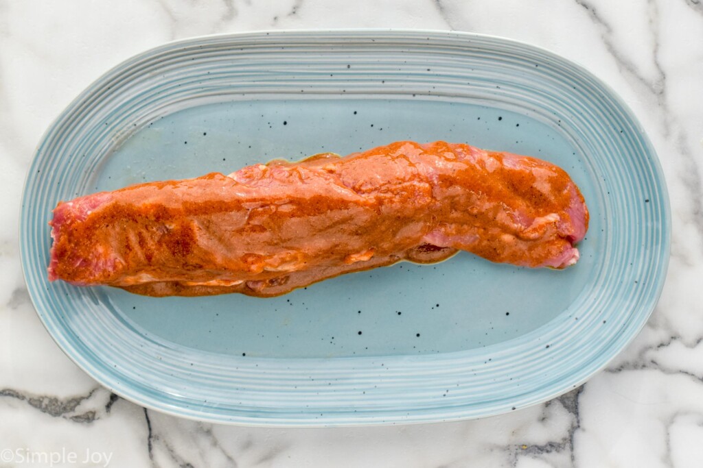 Overhead view of pork tenderloin covered in sauce on a platter before cooking for Air Fryer Pork Tenderloin recipe.