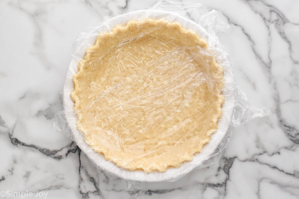Overhead view of pie crust in pan with plastic wrap covering it for how to blind bake a pie crust recipe