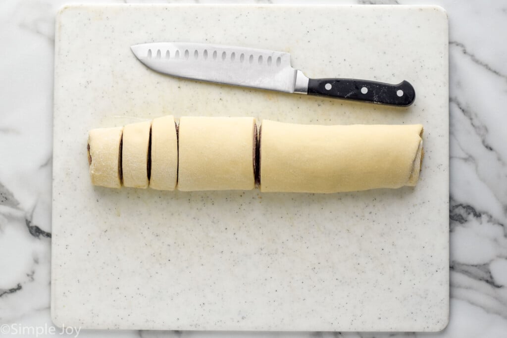 overhead of cinnamon roll dough rolled up and cut with knife laying beside