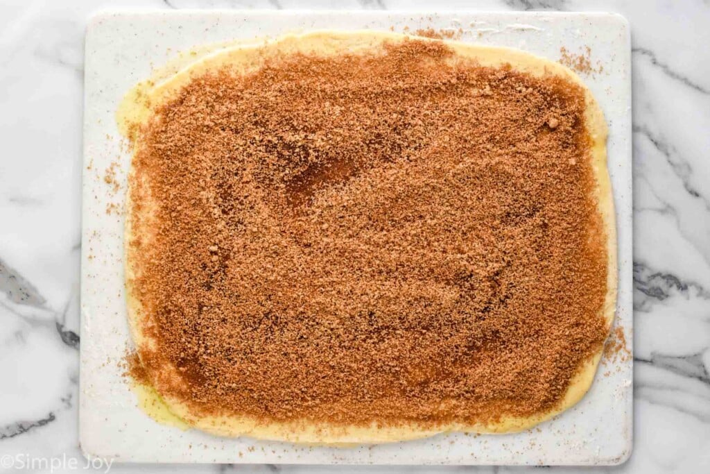overhead of cutting board with homemade cinnamon roll dough rolled out and topped with butter and brown sugar mixture